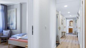 A modern bedroom with a bed, a chair, a painting, and a hallway leading to a bathroom.