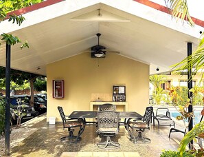 Eine Außenpatio mit überdachtem Tisch und Stühlen, einem Deckenventilator und einem gefliesten Boden.