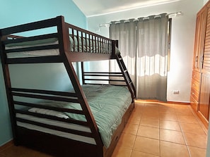 Ein Stockbett in einem Zimmer mit gefliestem Boden, einem fenster mit Vorhängen und einem Holzschrank.