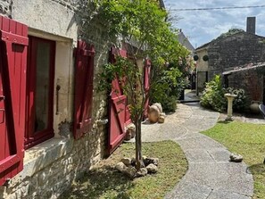 A stone building with red shutters, a narrow pathway, and a small tree. - Authentic Charente house in a quiet natural area (La Villedieu)