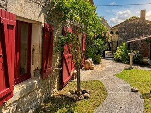A stone building with red shutters, a small tree, and a stone pathway leading to another building. - Authentic Charente house in a quiet natural area (La Villedieu)