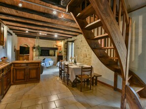 Ein rustikales Interieur mit freiliegenden Holzbalken, einem Steinkamin, einem Essbereich und einer Holztreppe.