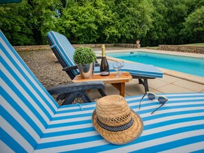 Ein Poolbereich mit gestreiften Liegestühlen, einem Tisch mit Flasche und Gläsern, einem Topfpflanzen und einem Strohhut.