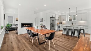Een moderne keuken met witte kasten, een centraal eiland en een eethoek met een houten tafel en zwarte stoelen.