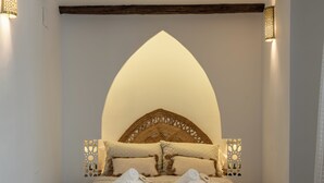 Un lit doté d’une tête de lit arquée originale, deux tables de chevet avec des lampes décoratives, et des serviettes soigneusement pliées posées sur le lit.