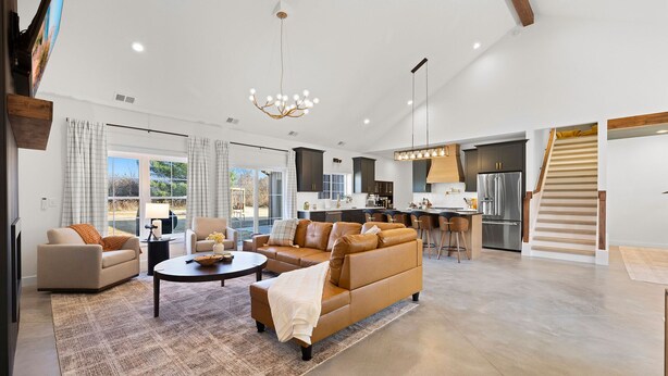 A spacious living area with a large sofa, a coffee table, and a dining table. There is a kitchen area with modern appliances and a staircase leading to an upper level. - Juniper Presents: NEW Luxe Stay w Hot Tub, Fire Pavilion Nr Lake MI (Berrien County)