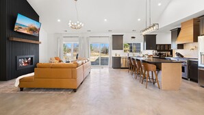 A modern kitchen with a central island, a dining area with bar stools, a living room with a sofa, and a fireplace. - Juniper Presents: NEW Luxe Stay w Hot Tub, Fire Pavilion Nr Lake MI (Berrien County)