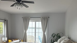 A bedroom with a bed, a ceiling fan, a window with curtains, a bedside table with a lamp, and a view of the outdoors. - Gorgeous 4 bedroom home , sitting on beautiful Davidson lake .. (Dumfries)
