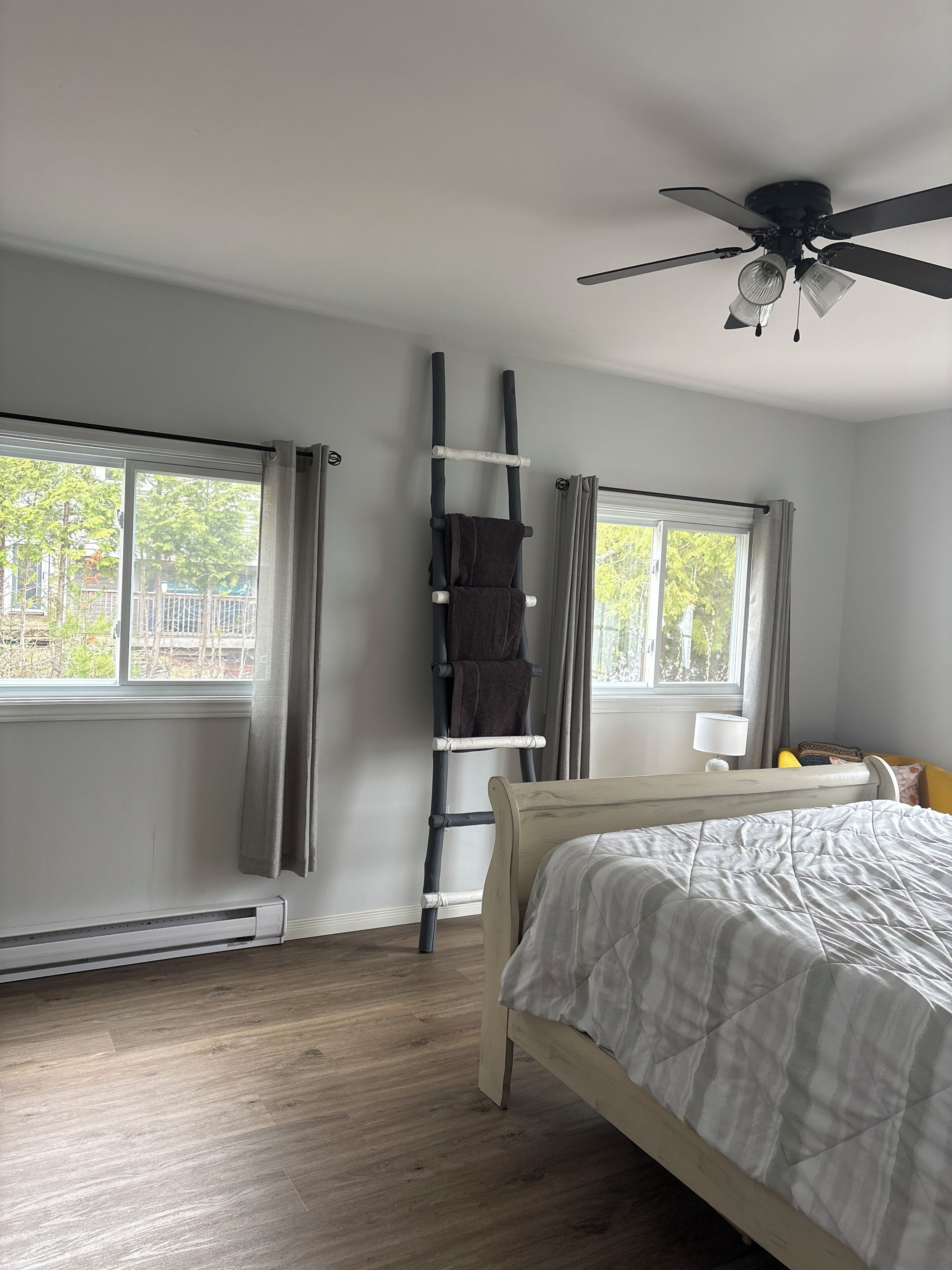 Ein Schlafzimmer mit einem Bett, einem Deckenventilator, einem Fenster mit Vorhängen und einer Heizung.