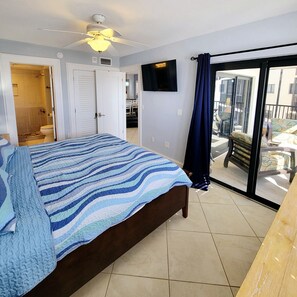 A bedroom with a bed, a ceiling fan, a TV, and a balcony with a chair. - The Carlos Pointe 521 (Fort Myers Beach)