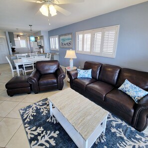 A living room with a brown leather sofa, a white coffee table, and a blue patterned rug. - The Carlos Pointe 521 (Fort Myers Beach)