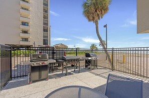 Une terrasse avec des barbecues, un palmier et un bâtiment en arrière-plan.