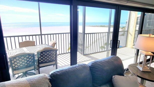 Un balcone con vista sulla spiaggia, un divano, una poltrona e un tavolo con una lampada.