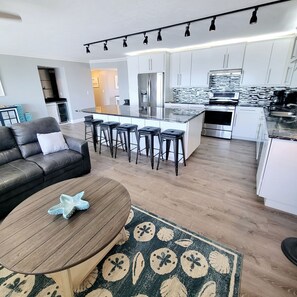 A modern kitchen with a central island, bar stools, and a dining area with a leather sofa and coffee table. - The Carlos Pointe PH1 (Fort Myers Beach)