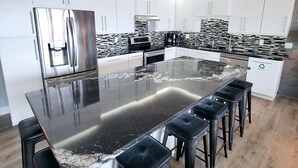 Una cucina moderna con una grande isola, sgabelli da bar, elettrodomestici in acciaio inossidabile e una parete di fondo bianco e nero.