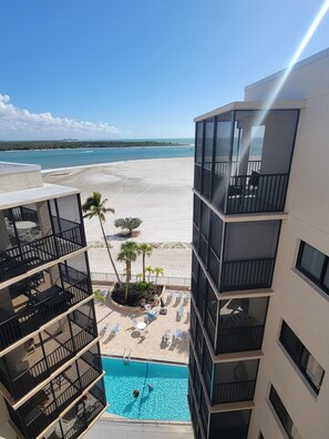 Ein Pool mit Blick auf den Strand, ein Gebäude mit Balkonen und ein klarer Himmel.