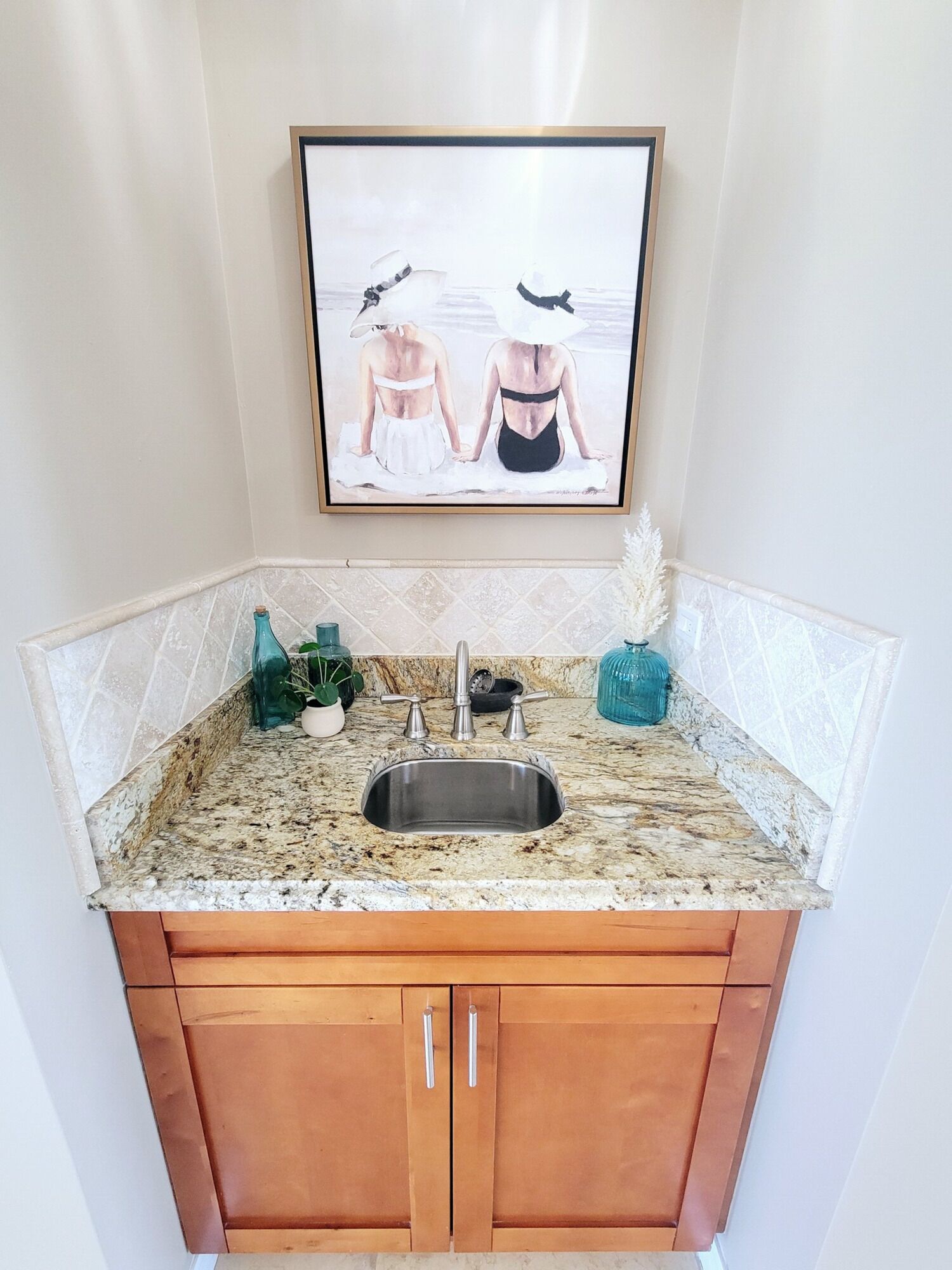 A kitchen with a granite countertop, stainless steel sink, wooden cabinets, and a framed picture above the sink.