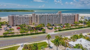 Un hotel de varios pisos con estacionamiento, una calle al frente y una playa al fondo.