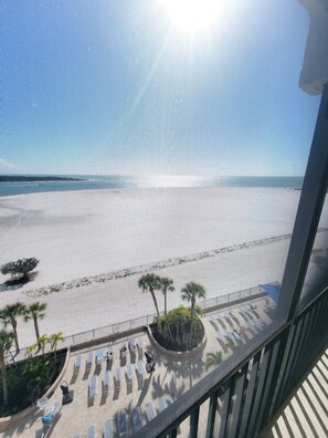 Blick auf einen Strand vom Balkon mit Geländer, Palmen und Liegestühlen.