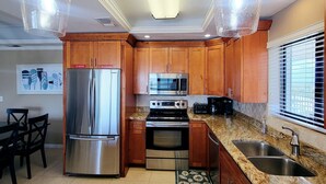 Una cocina con encimeras de granito, electrodomésticos de acero inoxidable, armarios de madera e iluminación colgante.