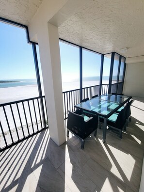 Un balcon avec une table et des chaises en verre, une vue sur la plage et un sol carrelé.