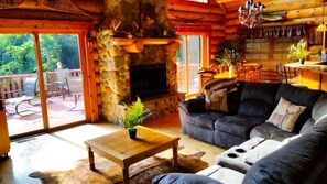 A log cabin interior with a stone fireplace, a leather sofa, and a dining area.