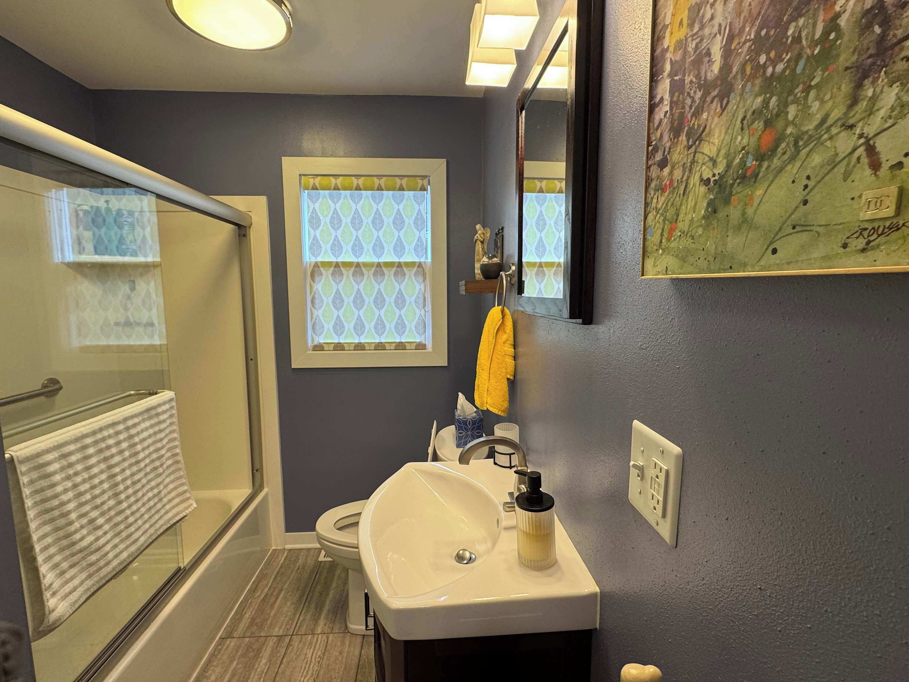 Un baño con cabina de ducha de vidrio, inodoro, lavamanos con dispensador de jabón y perchero para toallas.
