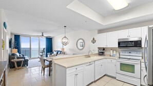 A modern kitchen with white cabinets, a large island, a microwave, oven, and a view to the outside. - Summerwind West 1403 - The Beach Fort (Navarre)