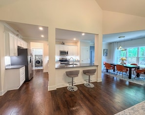 Een moderne keuken met een centraal eiland, een eethoek met tafel en stoelen, en een uitzicht op de natuurlijke omgeving door grote ramen.