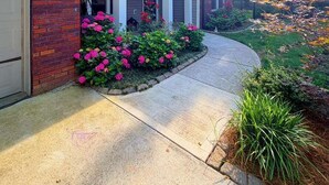 A two-story house with a brick facade, a covered porch, and a landscaped garden with pink flowers. - Spacious 5BR Home / Fenced Backyard / Fire pit / Fast Wi-Fi (Indian Trail)