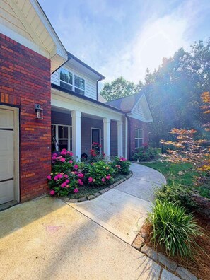 A two-story house with a brick facade, a covered porch, and a landscaped garden with pink flowers.