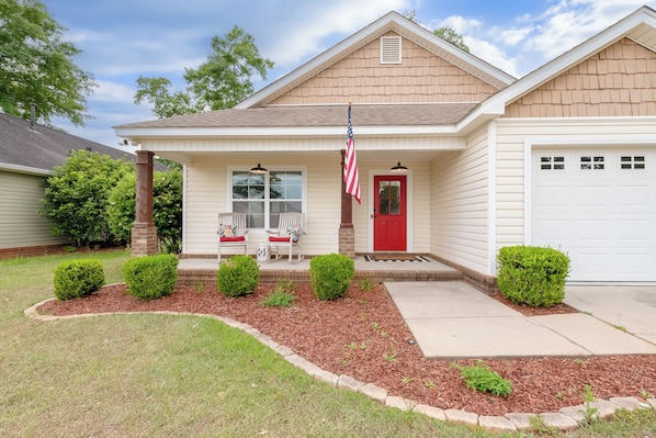 A residential house with a front porch, a red door, and an American flag.