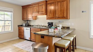 Una cocina con armarios de madera, encimera de granito, cafetera y lavavajillas.