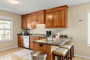 A kitchen with wooden cabinets, a granite countertop, a coffee maker, and a dishwasher. - Winterberry- Manor 3BR King+Queen  85"TV  Base (Enterprise)