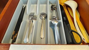 A drawer with compartments containing chopsticks, forks, spoons, a knife, and a pair of scissors.
