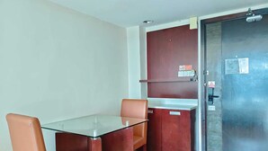 A small room with a glass-top table and two chairs, a wooden cabinet, and a door with a handle.