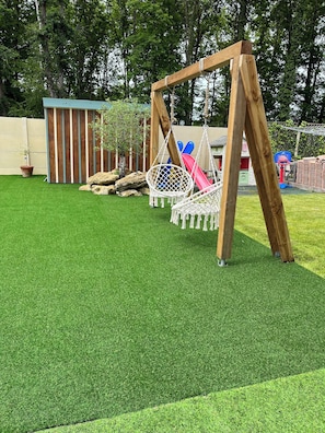 A wooden swing set, a white hanging chair, and a small shed in a backyard with artificial grass. - Villa with heated pool - 3 bedrooms - Bassin d'Arcachon - France (Mios)