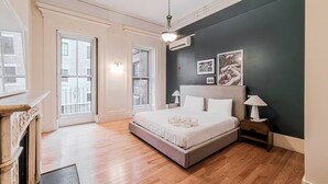 A bedroom with a bed, bedside tables, a nightstand, a fireplace, and a view of the outside. - Beacon Hill - Historic Elegance (Boston)