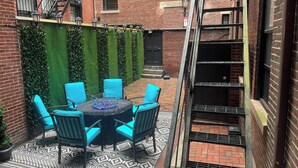 A brick building with a courtyard featuring a round table with chairs, a patterned rug, and a green wall with climbing plants. - Beacon Hill - Historic Elegance (Boston)