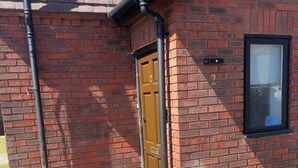Un bâtiment en briques avec une porte marron, une fenêtre et un tuyau noir.