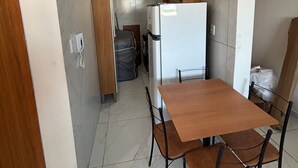 Ett kompakt kök med ett träbord och stolar, ett vitt kylskåp och en kakelbeklädd vägg bakom arbetsbänken.