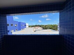 A view through a window with blue-tiled walls, a clear sky, and a building with a blue facade. - Cozy apartment close to the best beaches in João Pessoa. (João Pessoa)