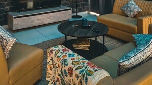 Un salon moderne avec un mur en briques, un téléviseur à écran plat posé sur une console en bois, un canapé, une table basse et un balcon doté d’une rambarde.