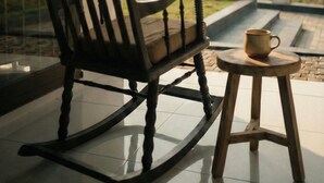 Une chaise berçante et un petit tabouret sur un balcon donnant sur un paysage verdoyant.