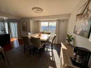 A dining area with a table, chairs, a coffee machine, and a view of the city.
