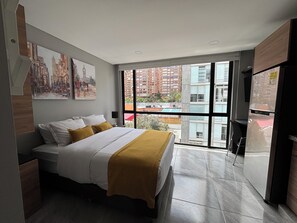 A modern hotel room with a large bed, a view of buildings through a glass door, and a refrigerator. - Usaquen FROM 124 (Bogotá)