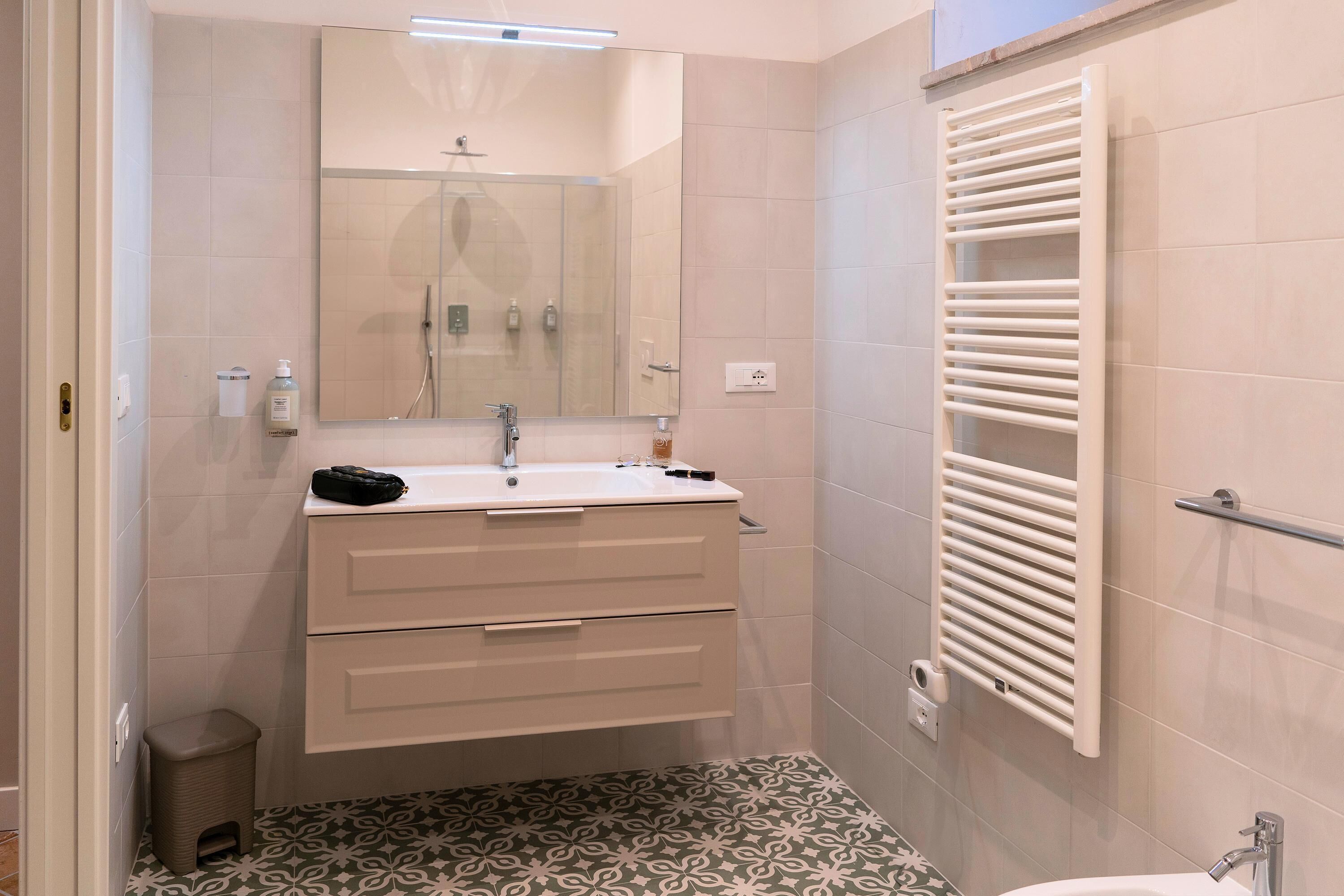 A bathroom with a sink, mirror, towel rack, and patterned floor tiles.