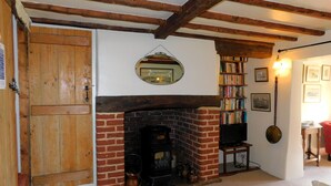 A room with a brick fireplace, wooden beams, a bookshelf, and a television. - Beechwood Cottage, Alby -  a quaint, rural cottage that sleeps 2 guests  in 1 bedroom (Alby)