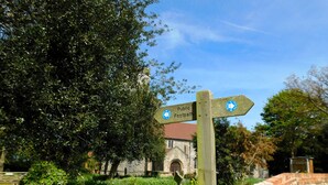 A wooden signpost with directional arrows, a stone wall, and a building with a red roof in the background. - Beechwood Cottage, Alby -  a quaint, rural cottage that sleeps 2 guests  in 1 bedroom (Alby)