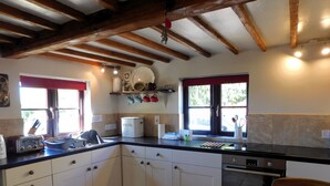 A kitchen with white cabinets, a bread maker, and a window with red curtains. - Beechwood Cottage, Alby -  a quaint, rural cottage that sleeps 2 guests  in 1 bedroom (Alby)
